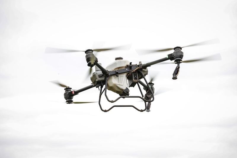 Close view of a large agricultural spray drone in flight against a pale sky